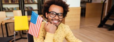 Student wearing glasses holding a United States flag in a library.