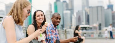Three students talking outdoors with a city skyline behind them.