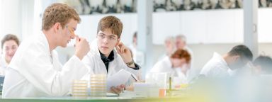 Two students in white lab coats examining samples in a laboratory.