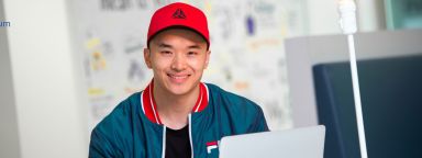 Student wearing a red cap seated at a computer workstation.
