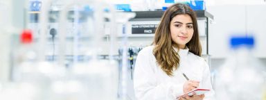 Woman in a white lab coat holding a notebook in a laboratory.
