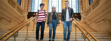 Three students walking down a staircase inside a university building.